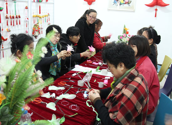 图为手工老师为居民如何利用废旧材料制作手工艺品进行耐心讲解,并